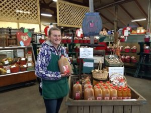 pine tree apple orchard cider being display in jugs by a female employee