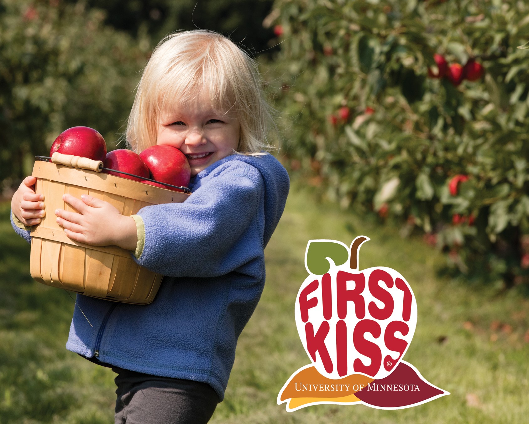 Little girl carrying a basket of apples with the logo First Kiss by University of Minnesota