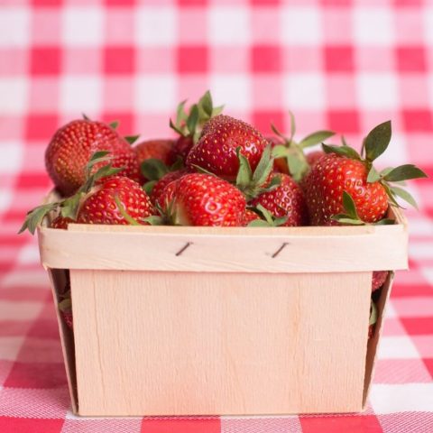 Strawberries in a wood basket on a picnic blanket