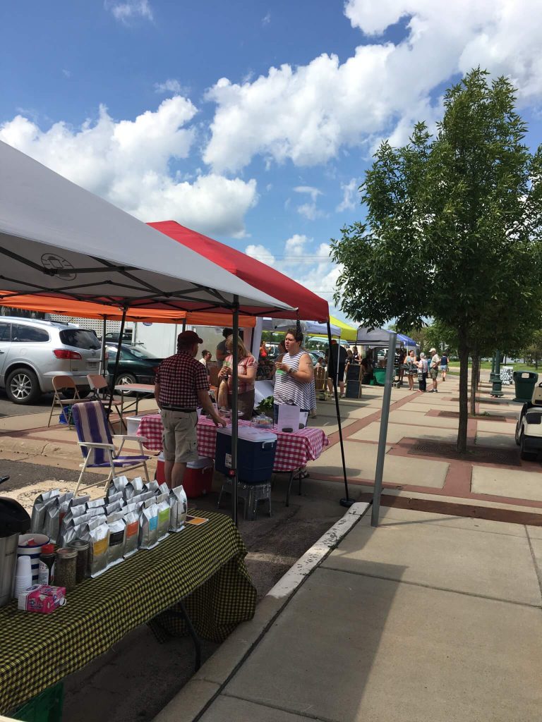 View of market stand with coffee, visitors in the distance.