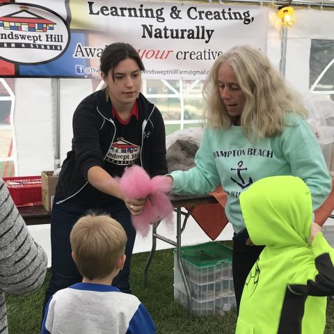 Two women showing dyed wool to young kids at a educational event