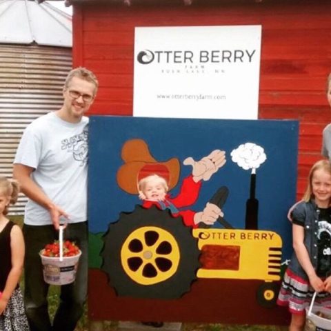 Family posin by the Otter Berry Sign that has a yellow tractor and waving man