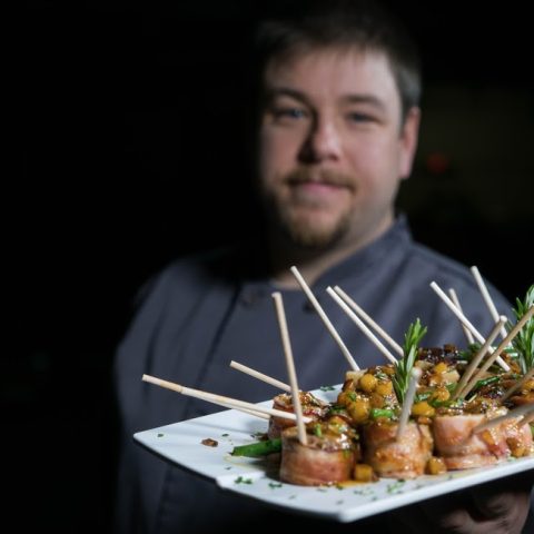 Chef holding a fancy bacon wrapped food with sticks
