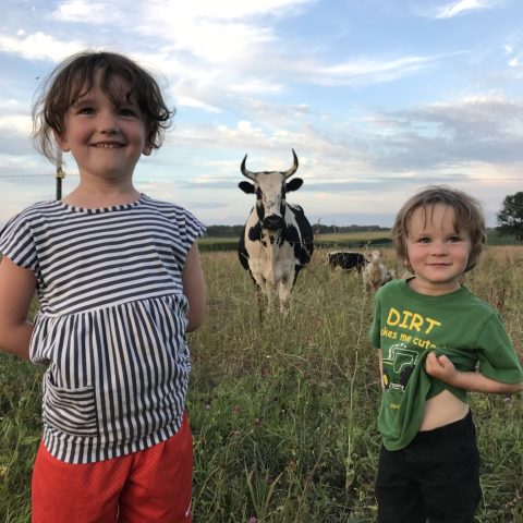 Two kids posing with a horned cow in the background