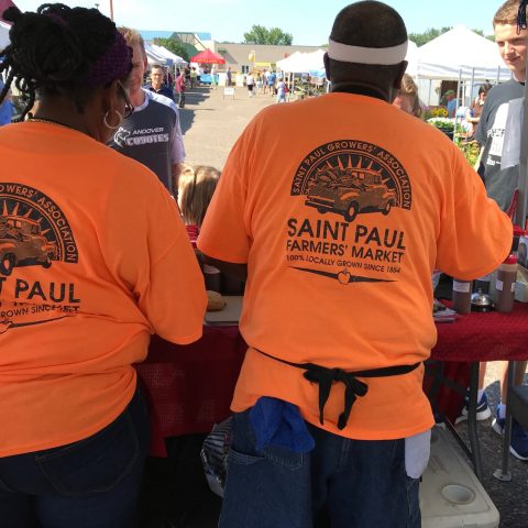 back of two peoples' shirts they say st paul farmers market association they are selling things