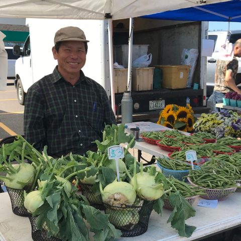 man smiling behind booth selling kohlrabi and green beans