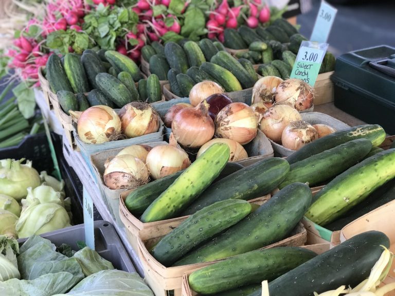 close up of cucumbers and yellow onions on a table among other veggies