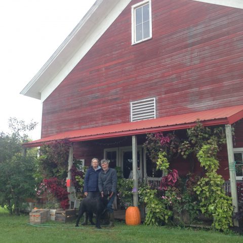 couple standing in front of large red barn with porch filled with flowers