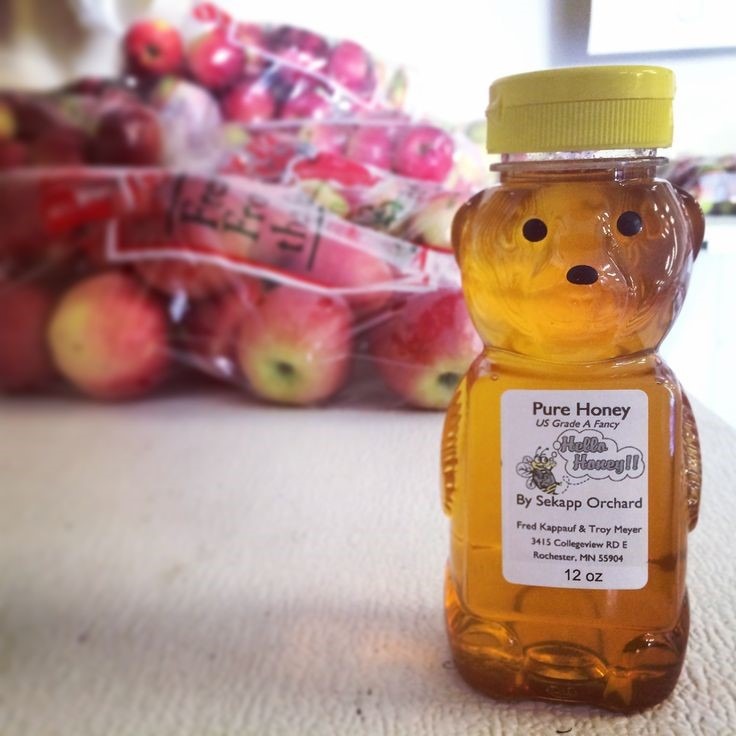close up of plastic honey bear honey bottle with bags of apples in the background