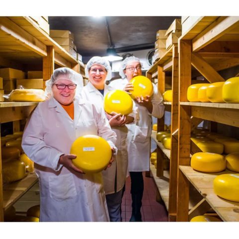 three women standing with wheels of cheese