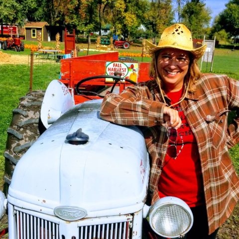 person leaning on light blue antique tractor in a straw hat and flannel