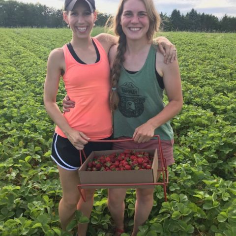 two people holding a flat of berries a strawberry field