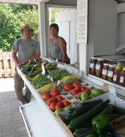 two people standing next to a stand full of produce