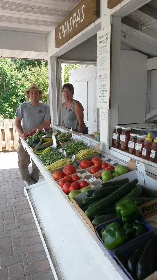 two people standing next to a stand full of produce