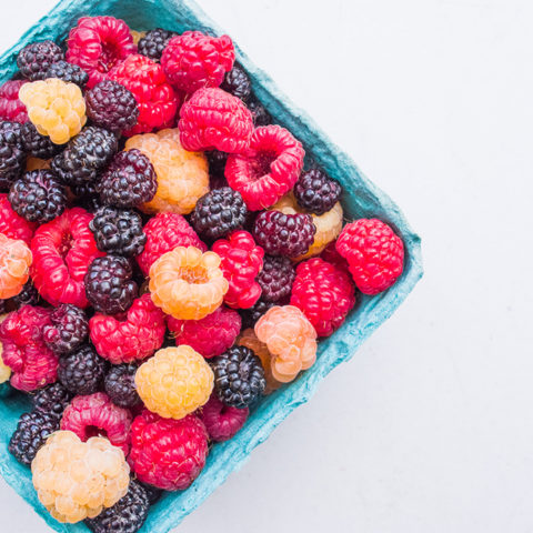 fresh golden, black, and red raspberries in a cardboard container