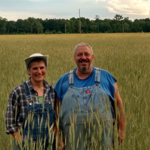 Husband and wife farmers standing in their field during summer