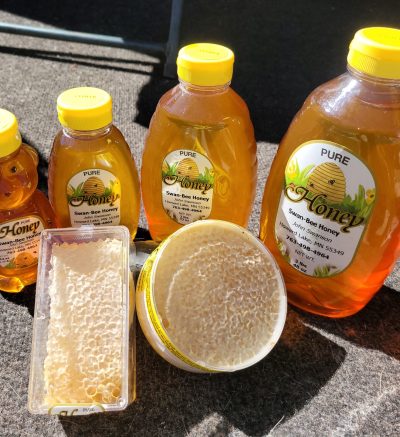 Photo of honey products on a table - containers of honecomb and honey bears and jars of honey in various sizes