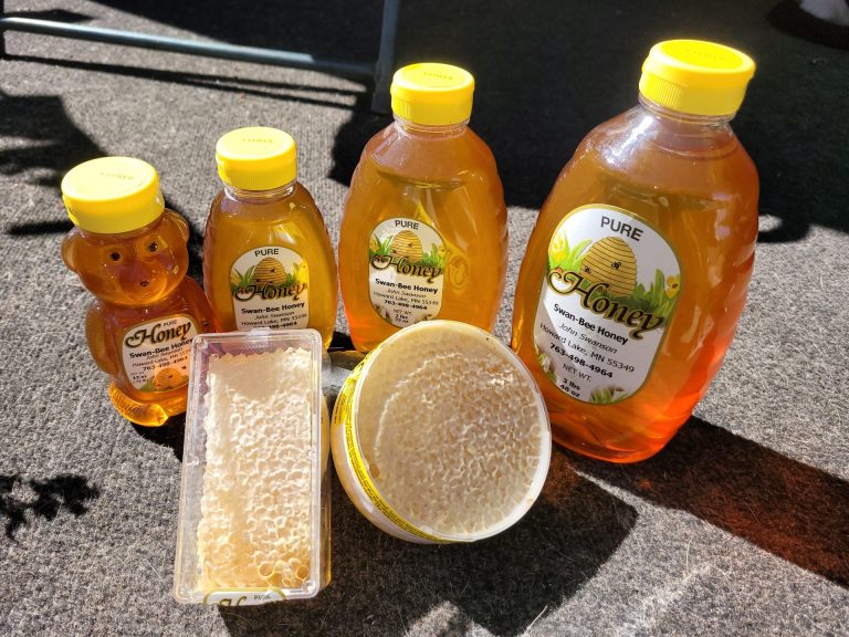 Photo of honey products on a table - containers of honecomb and honey bears and jars of honey in various sizes