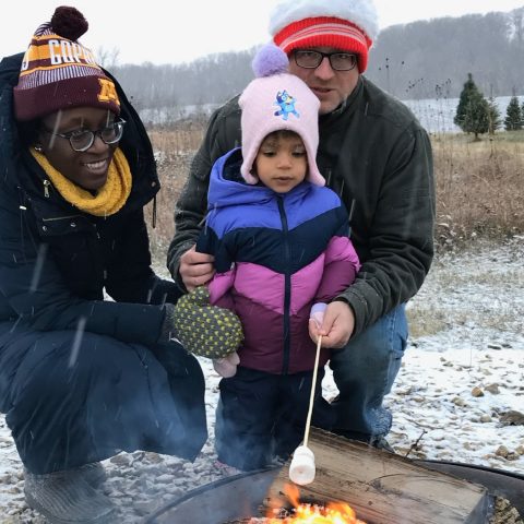 Picture of a man and woman with a young child roasting marshmallows on a bonfire.