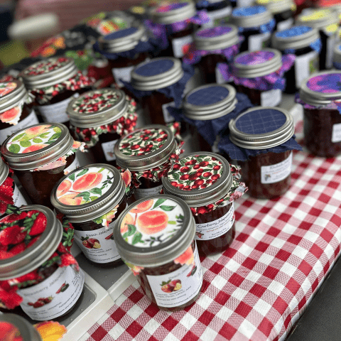 Picture of jars of jellies and jams on a table with a red plaid tablecloth.