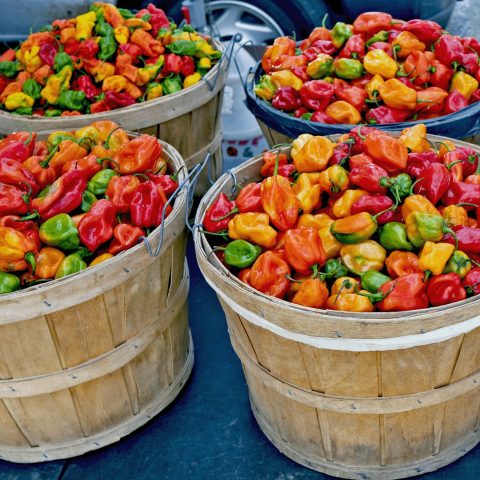 Wood baskets filled with small red, orange, yellow, and green peppers.