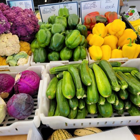 Array of fresh yellow and green peppers, zucchini, green and red cabbage, and white and red cauliflower on a table.