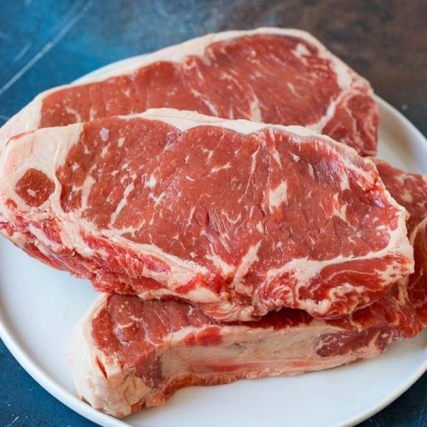 Cuts of red, raw meat on a white plate.