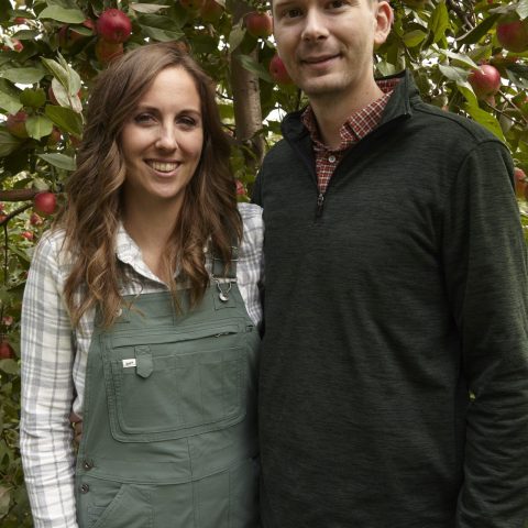 Picture of a young couple smiling with an apple tree behind them.