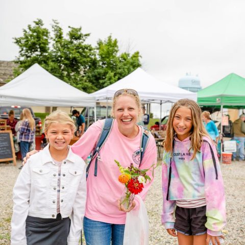 A smiling woman and girls at a farmers market.