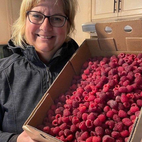 A woman holding a large cardboard flat filled with raspberries.