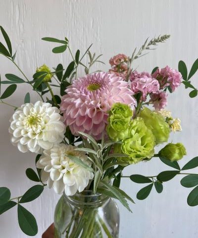 Picture of a bouquet of light pink, white, and light green flowers with dark green foliage in a clear vase.