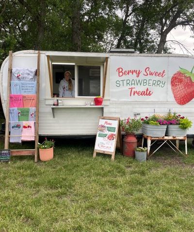 Picture of a food truck selling treats. The food truck says "Berry Sweet Strawberry Treats" and there is a woman smiling inside the truck.