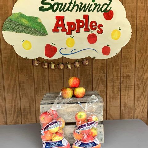 Sign for Southwind Apples with two bags of apples sitting below it and a few apples stacked on a wooden crate