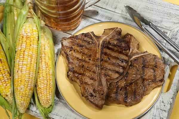 Grilled beef tbone steak on a plate alongside ears of sweet corn