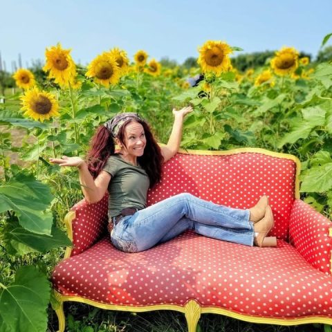 A woman at a photo-op station sitting on a vintage couch in a sunflower field.