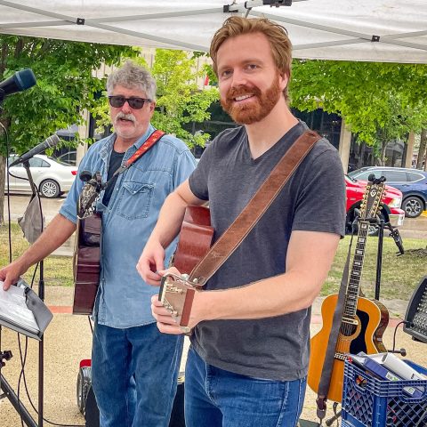 two men hold guitars and smile at the camera