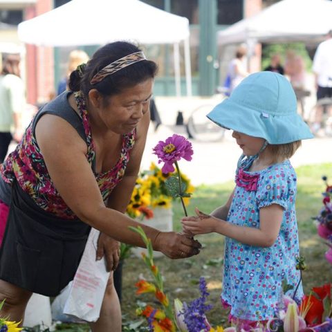woman bends down to hand a small girl a pink flower