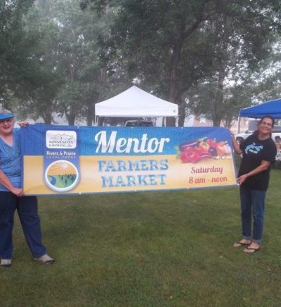 two people holding up a mentor farmers market banner