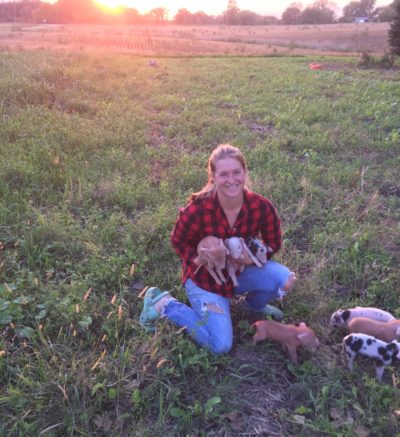 woman holding piglets in front of a sunset