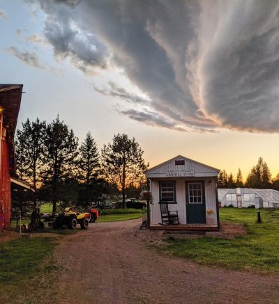 Evening scene of a red barn and small red general store with hoop houses in the distance.