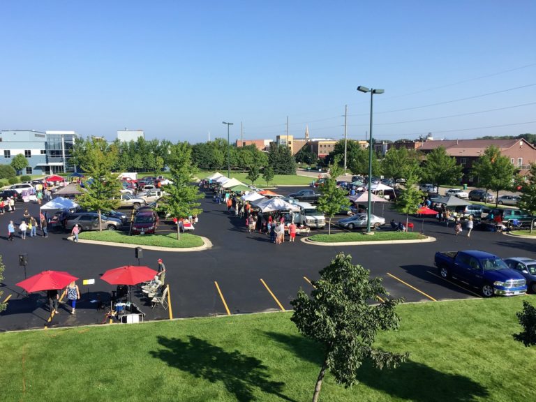 overview of outdoor market tents set up in a parking lot on a clear summer day