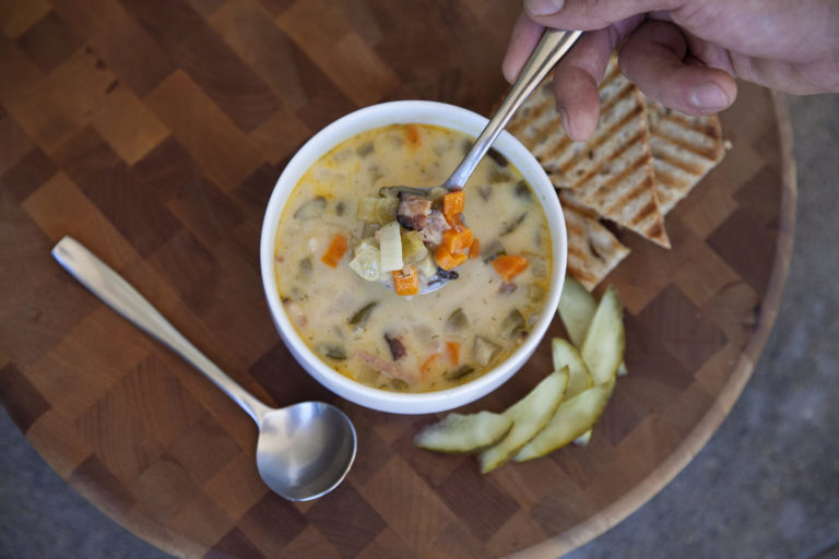 bowl of creamy soup with chunks of carrots and pickles with toasted bread on the side