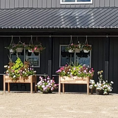 Picture of the Greensted storefront. The building is black and has hanging pots of flowers.