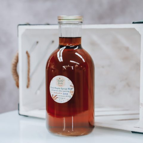 A bottle of maple syrup sits on a white platform with a white background behind it.