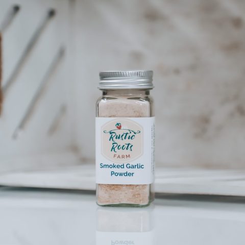 A labeled bottle of smoked garlic powder sits on a white platform against a white backdrop