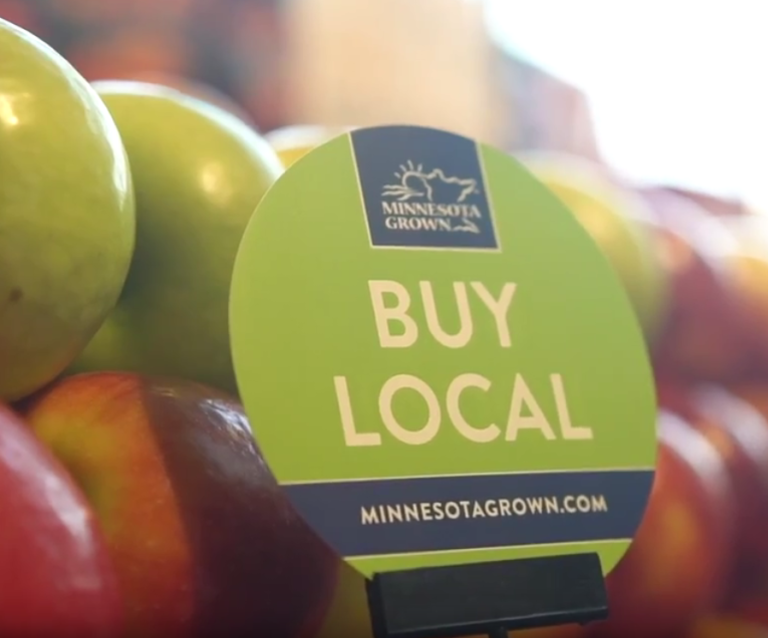 Green and blue sign saying "buy local" next to apples.