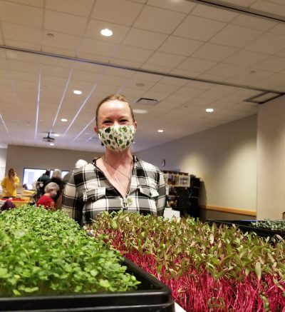 Person standing behind table filled with trays of microgreens