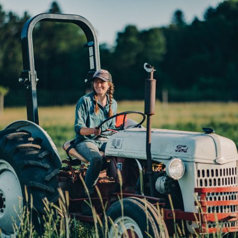 Person on a gray and red tractor outside with a field in the background