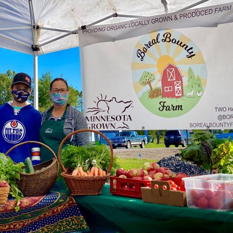 Member farm Boreal Bounty stands in front of farmers market banner purchased through cost share program.