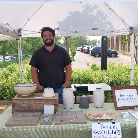 A man stands at a farmers' market stand. The stand is for Phillips Farmstead